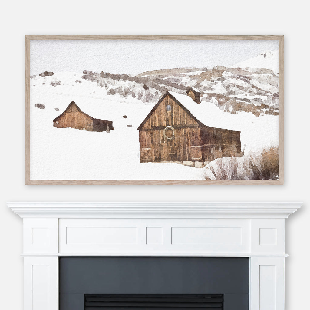 Watercolor winter landscape painting of two snowy wooden cabins in the mountains displayed in Samsung Frame TV above fireplace