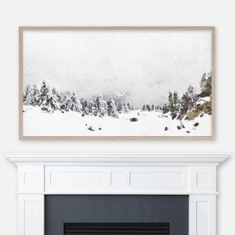 Watercolor winter landscape painting of foggy snow covered hill and pine trees displayed in Samsung Frame TV above fireplace